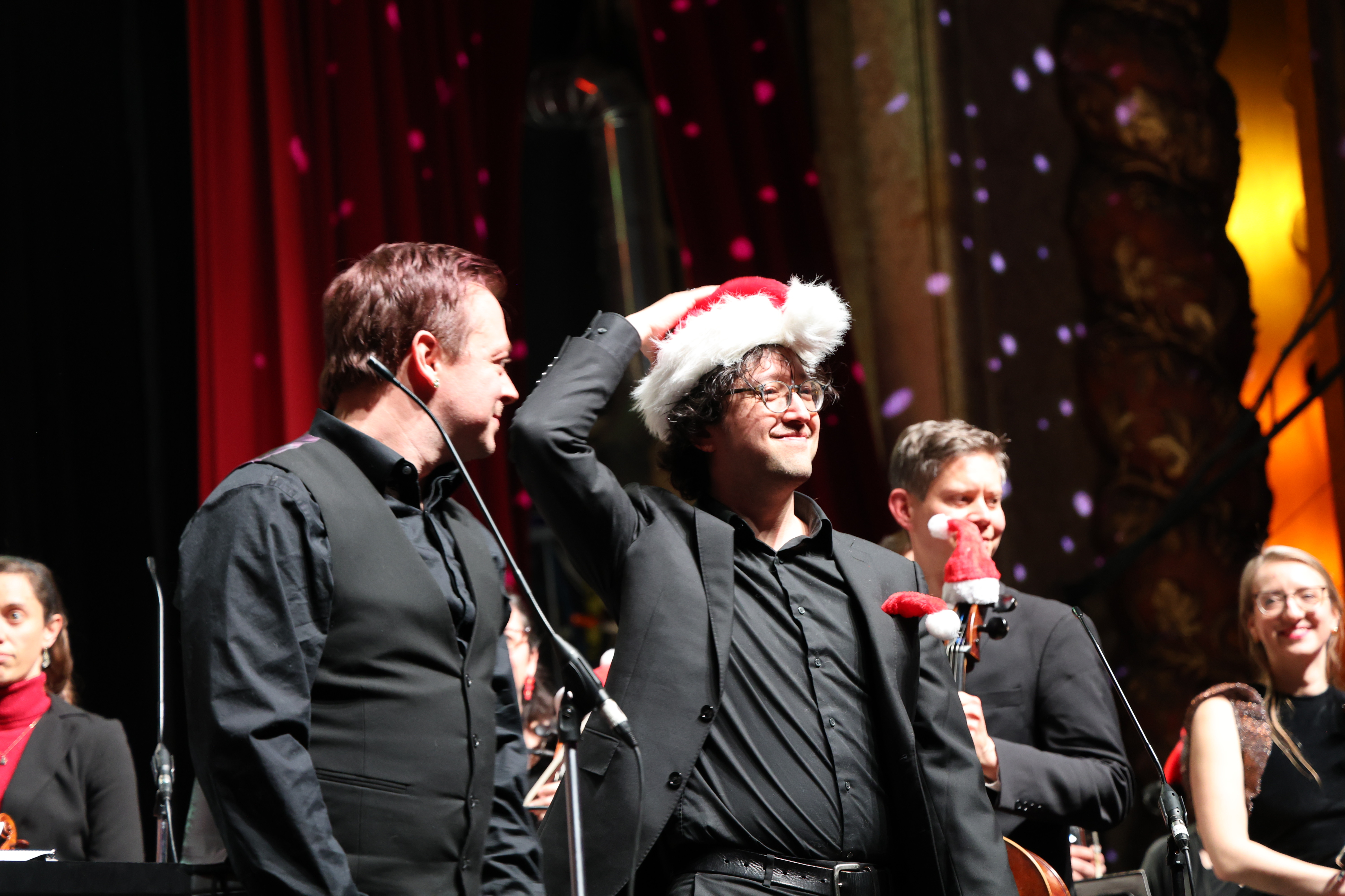 Photograph of orchestra members wearing Santa hats on stage.
